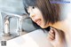 A woman is drinking water from a faucet in a bathroom.