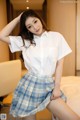 A woman in a white shirt and blue plaid skirt posing on a bed.