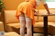 A woman in an orange skirt and white stockings bending over a table.