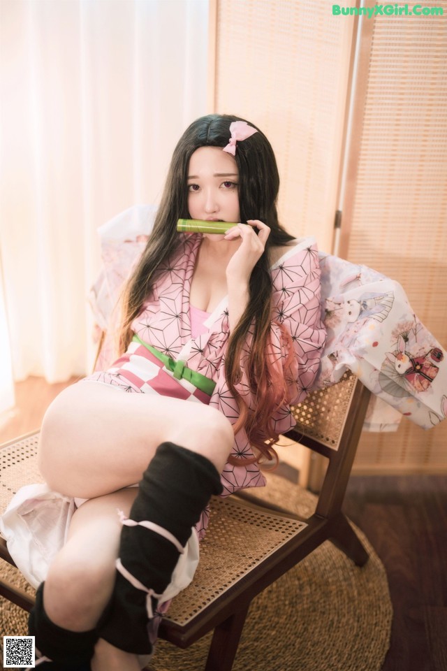 A woman in a pink kimono sitting on a chair.