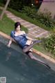 A woman in a blue dress and black stockings laying on the edge of a pool.