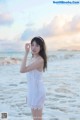 A woman in a white dress standing on the beach.