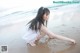 A woman in a white dress is sitting on the beach.