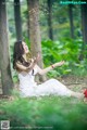 A woman in a white dress sitting on the ground in the woods.