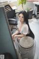 A woman sitting on top of a desk next to a fan.