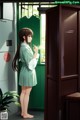 A girl standing in front of a green door holding a cigarette.