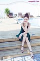 A woman in a green dress sitting on a wooden deck next to a pool.