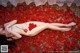 A naked woman laying on a bed of red rose petals.