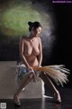 A naked woman sitting on top of a box holding a broom.