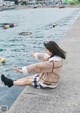 A woman sitting on the edge of a pier by the water.