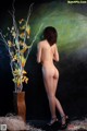 A naked woman standing next to a vase of flowers.