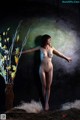 A naked woman standing next to a vase of flowers.