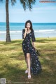 A woman in a black dress standing on a grassy field next to the ocean.