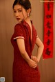 A woman in a red cheongsam poses for a picture.