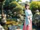 A woman in a pink and blue kimono standing in front of a pond.