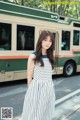 A woman in a striped dress standing in front of a bus.