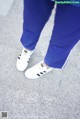 A person wearing blue pants and white sneakers standing on a sidewalk.