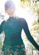 A woman in a green turtle neck sweater and floral skirt.