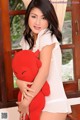 A woman in a white dress holding a red teddy bear.