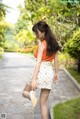 A woman in a white skirt and orange top is walking down a path.