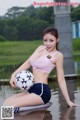 A woman in a pink top and blue shorts holding a soccer ball.