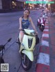 A woman sitting on a motor scooter on a city street.