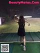 A woman in a black dress swinging a golf club.