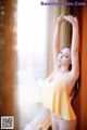 A woman in a yellow tank top standing by a window.