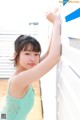 A woman in a green tank top leaning against a wall.