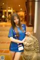 A woman in a blue dress posing next to a statue.