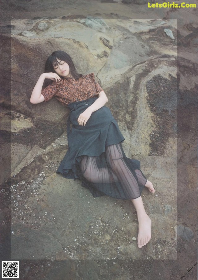 A woman laying on a rock on the beach.