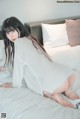 A woman in a white sweater is sitting on a bed.