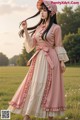 A woman in a pink dress and hat standing in a field.