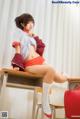 A woman sitting on top of a desk next to a red suitcase.